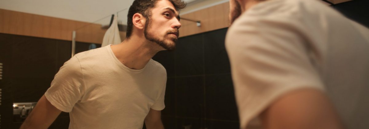stylish-concentrated-man-looking-in-mirror-in-bathroom-3771081